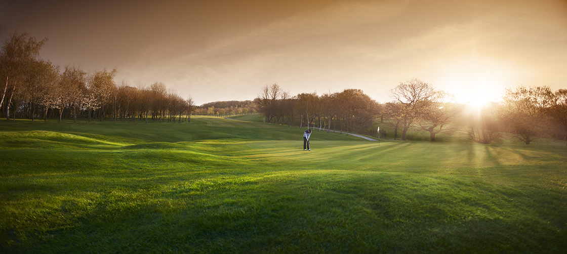 backlit golf course with golfer putting on a green